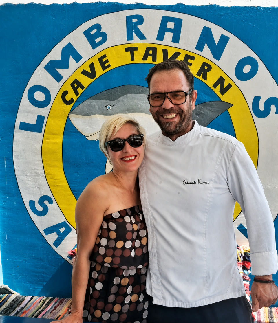 Two people standing in front of the hand-painted Lombranos Cave Tavern sign.