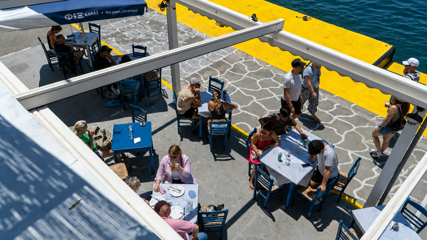 Lombranos seaside terrace with blue tables beside a yellow quay and the water.